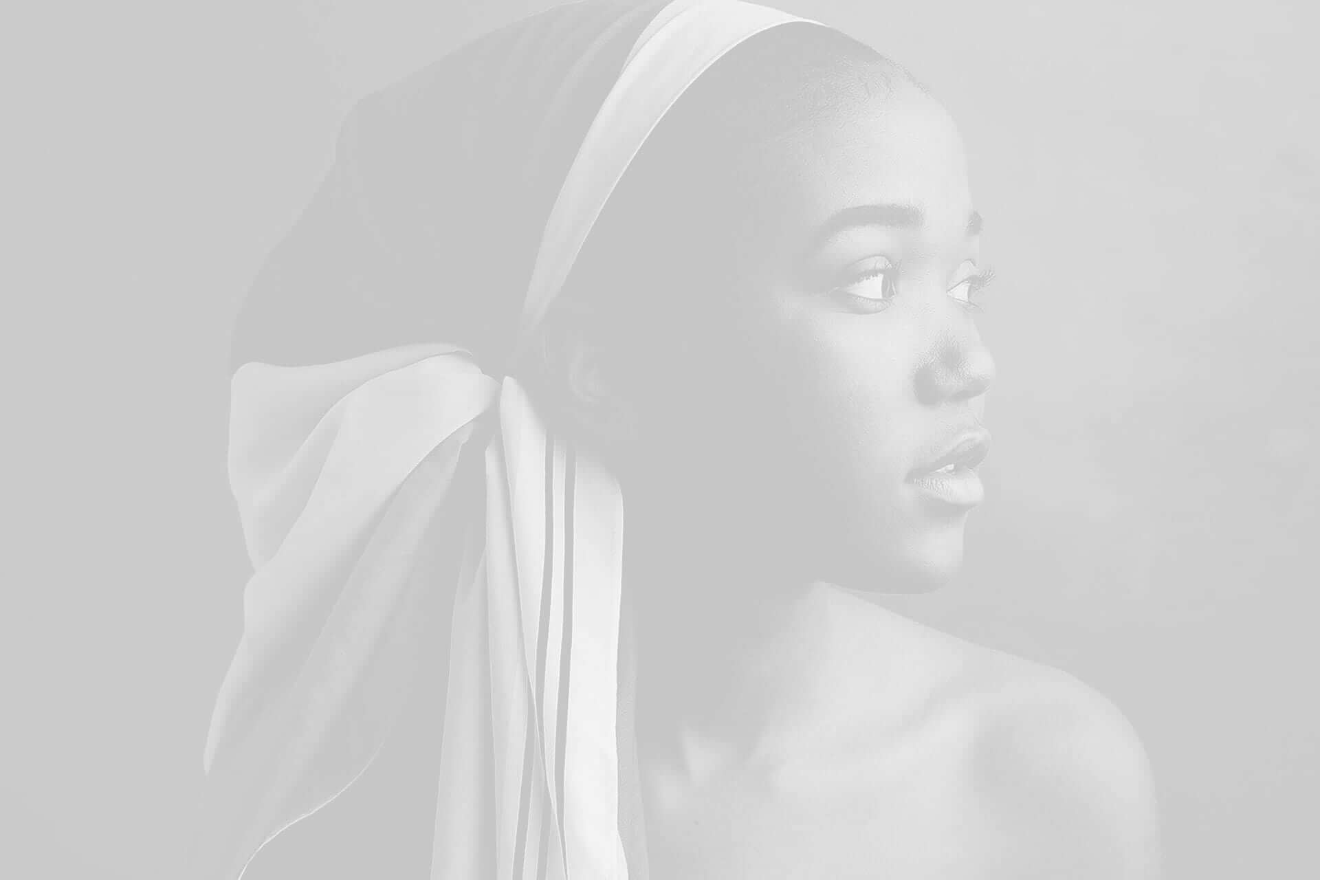Black and white portrait of a young woman with a headscarf looking to the side, against a grey background.