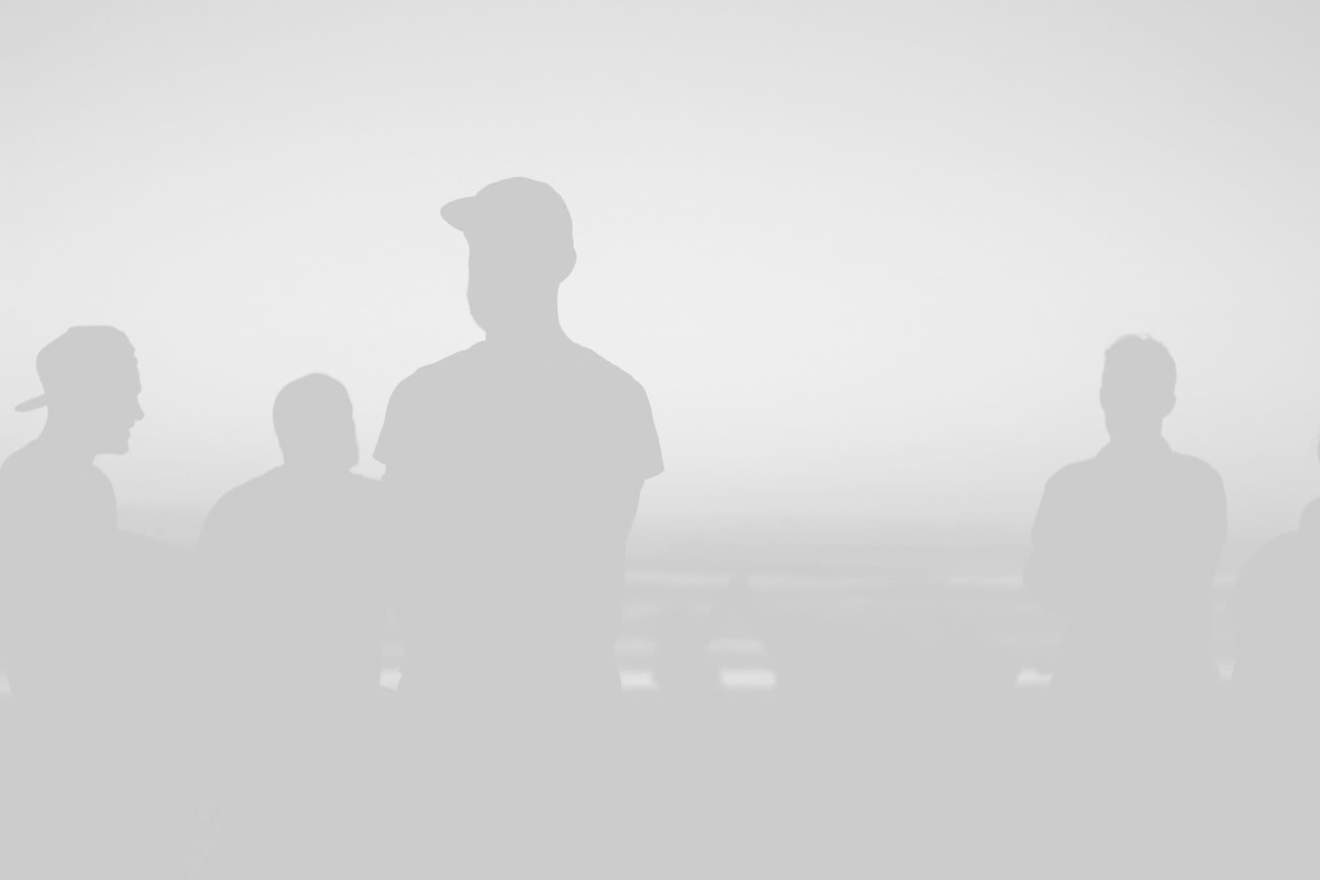 Silhouettes of several people, one prominently in a cap, against a softly illuminated white background.