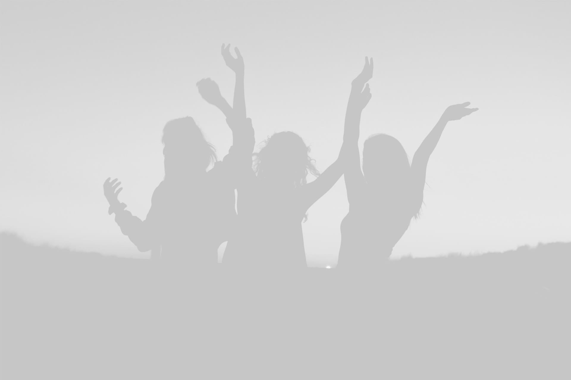 Silhouettes of three people with raised arms, joyfully posing against a bright, backlit background.