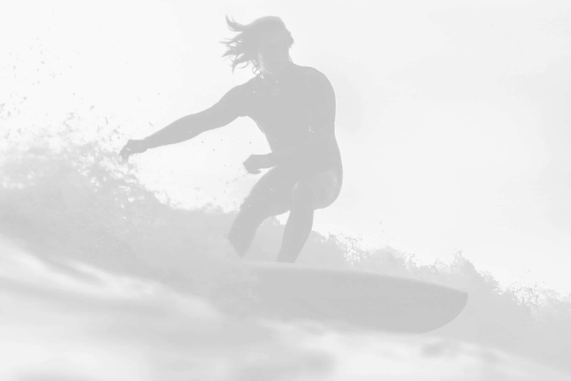 A silhouette of a surfer riding a wave, captured in a high-key, monochrome style.