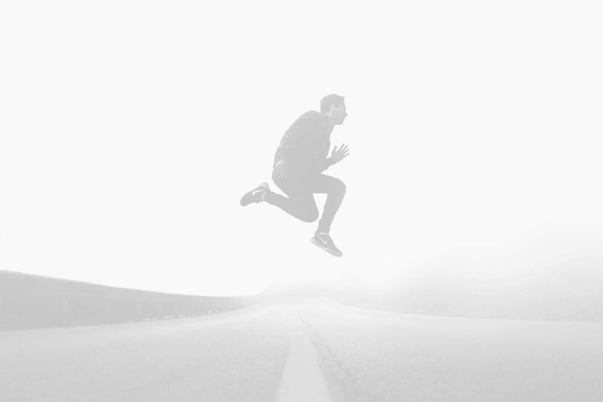 A man in a suit appears to levitate above a foggy road, captured in mid-air with a stark white background.