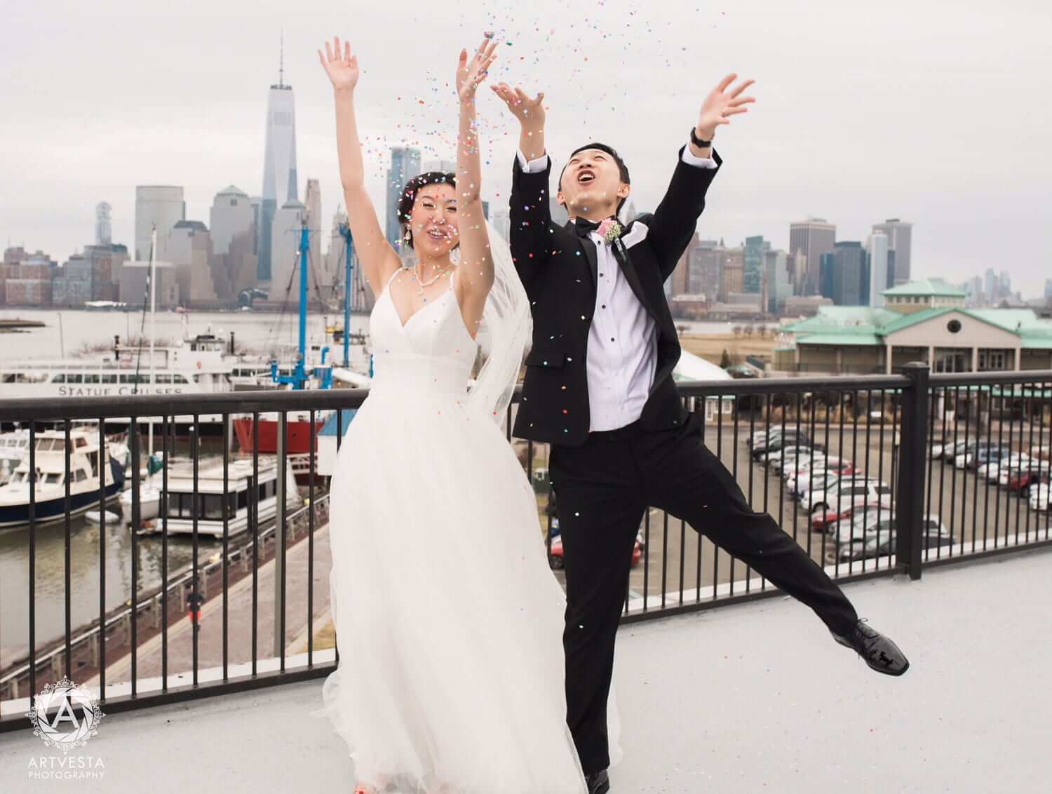 A joyful bride and groom jumping and throwing confetti on a rooftop with a city skyline in the background.