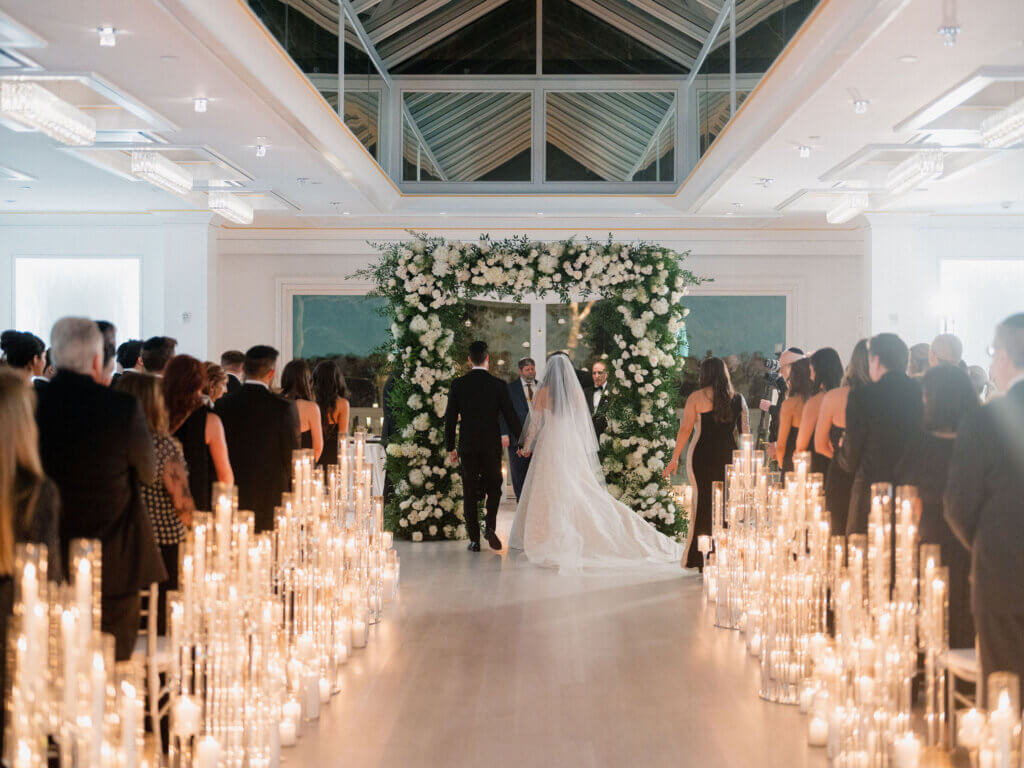 A Jewish wedding ceremony held under a floral arch with candles lining the aisle.